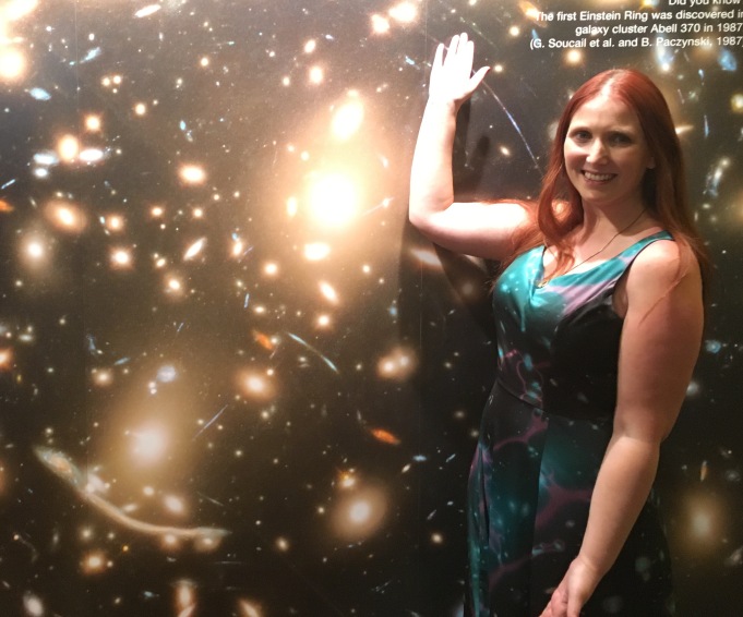 Wearing an astronomically themed dress of her own creation, Rachael poses in front of a large picture of Abell 370.